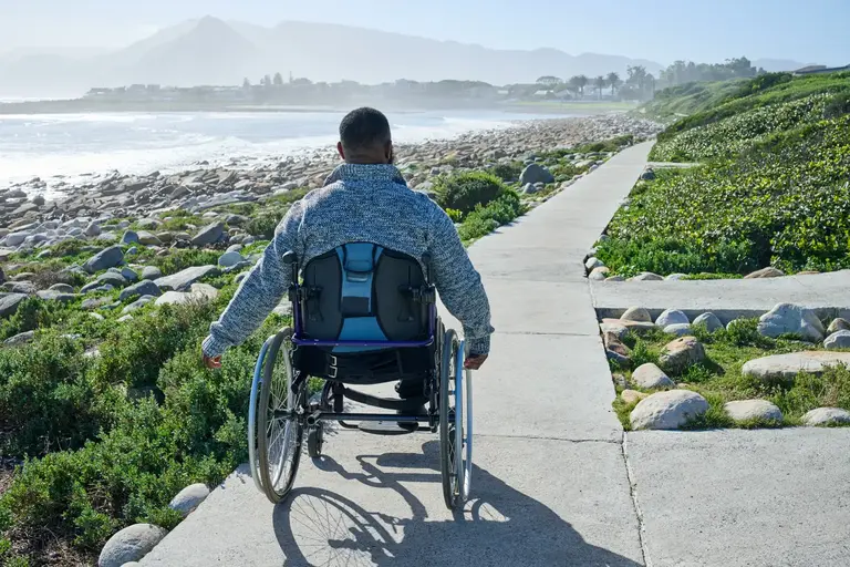 Man in wheelchair enjoying the sunshine on a path overlooking the beach